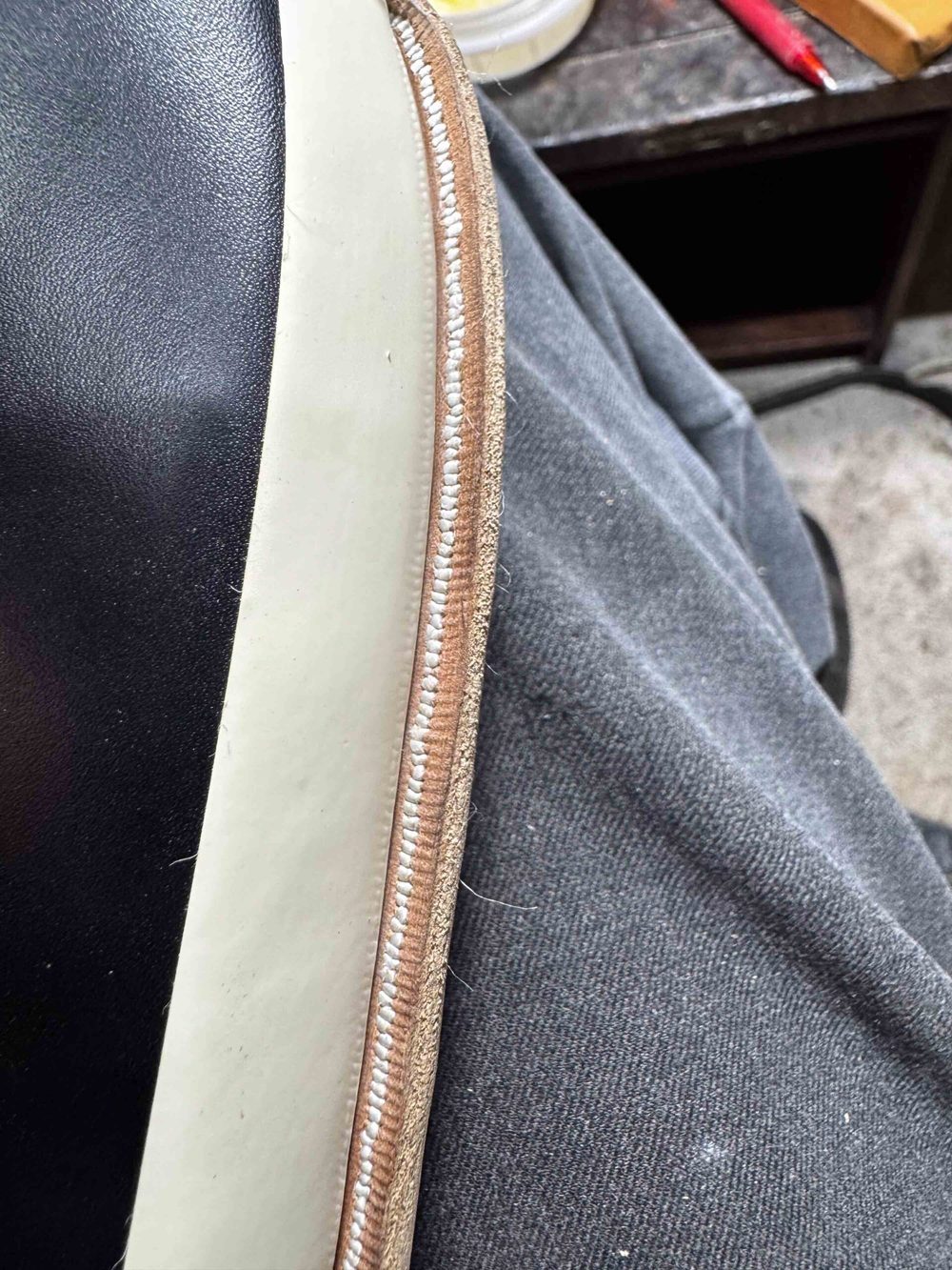 Close-up of a shoe edge showing black leather, a white stitching line, and a beige welt.