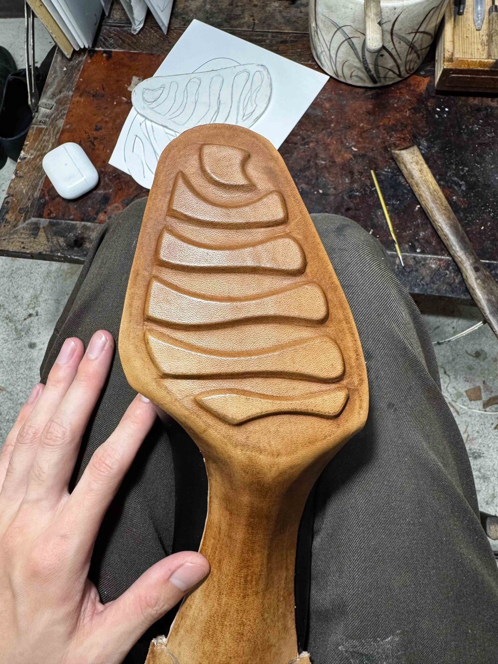 A hand rests on a brown, textured shoe sole featuring curved grooves and lines.