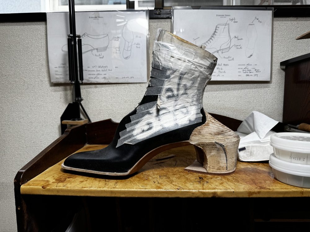 A black and wooden shoe prototype with a high heel, partially wrapped in tape for construction.