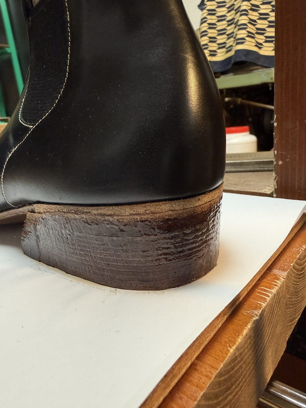 A close-up of the heel of a black leather shoe, featuring a dark brown wooden heel.