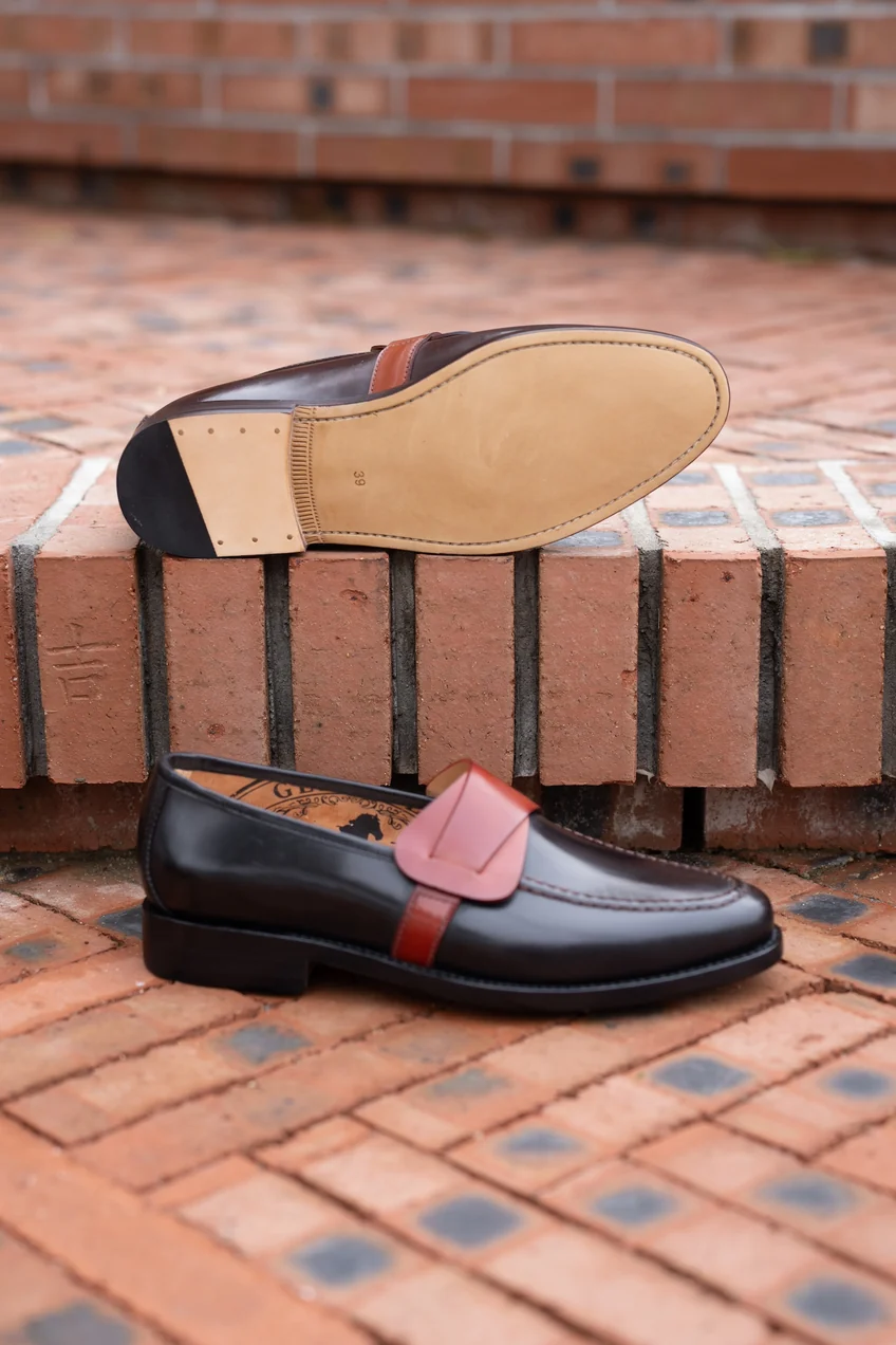 A pair of black cordovan shoes with a brown leather strap and a smooth sole.