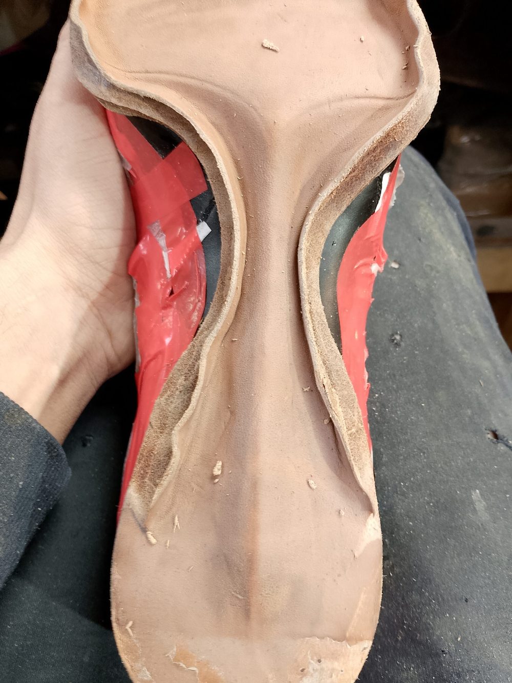 A hand holds a red shoe sole with a smooth, curved surface and visible texture.