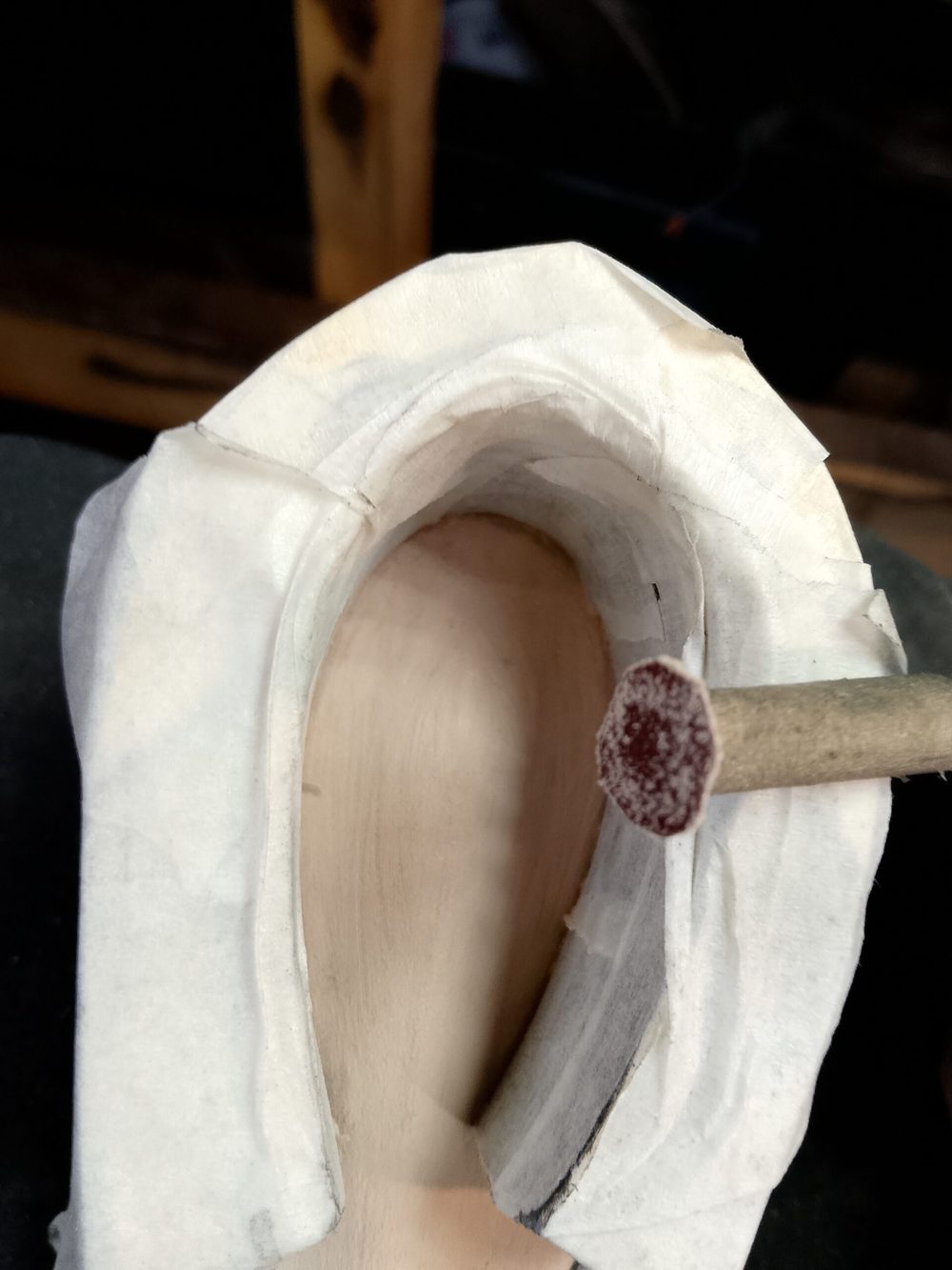 A wooden shoe last is partially wrapped in white tape, with a sanding tool inserted into its opening.