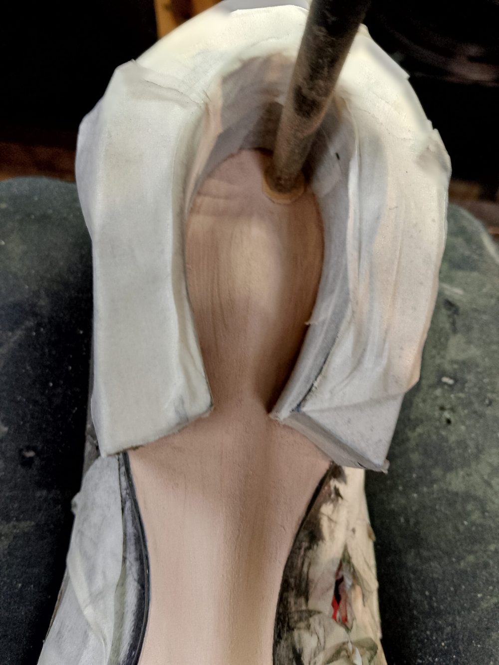 A close-up view of the interior of a shoe, featuring a light wooden base and white fabric lining.