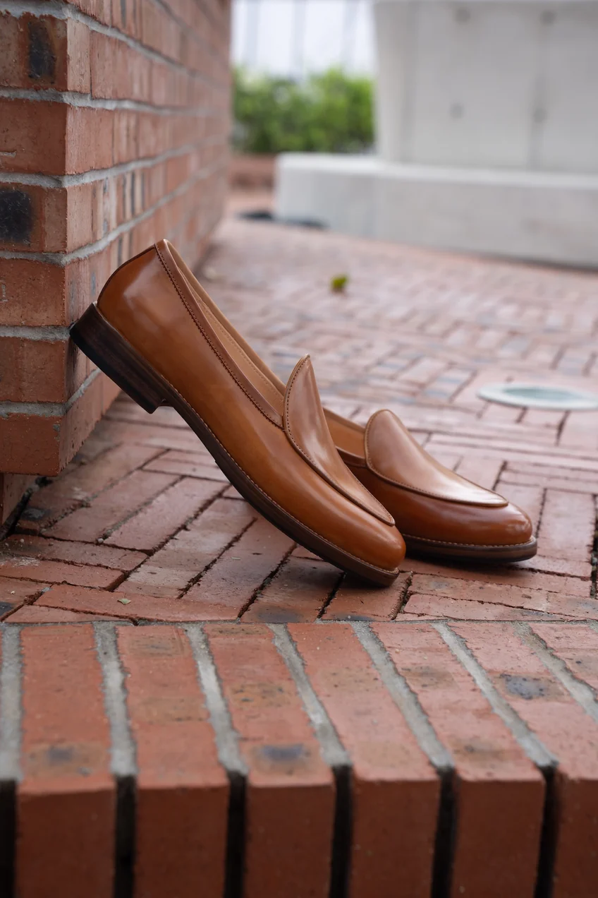 A pair of polished tan cordovan loafers resting on a brick surface.