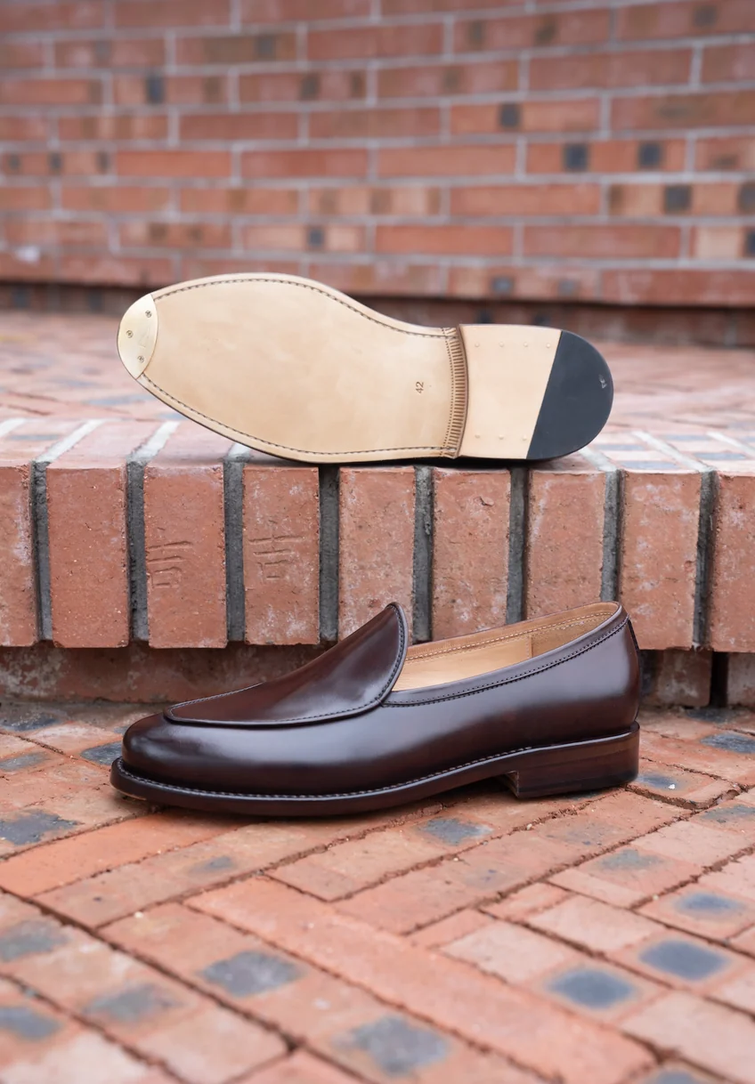 A brown leather slip-on shoe with a smooth finish and a light-colored sole.