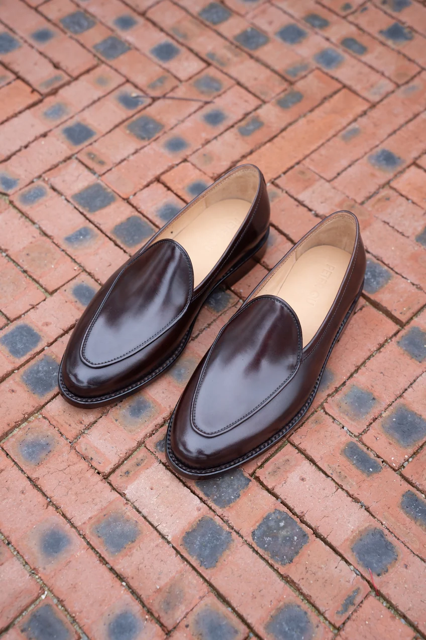 A pair of shiny, dark brown cordovan loafers with a sleek design.