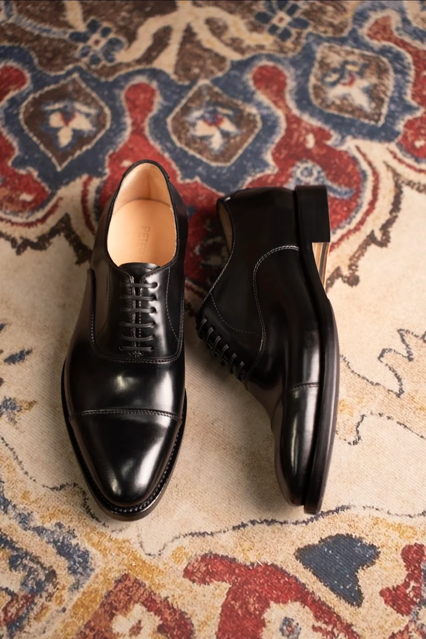 A pair of polished black leather dress shoes with lace-up design and cap toe detail.