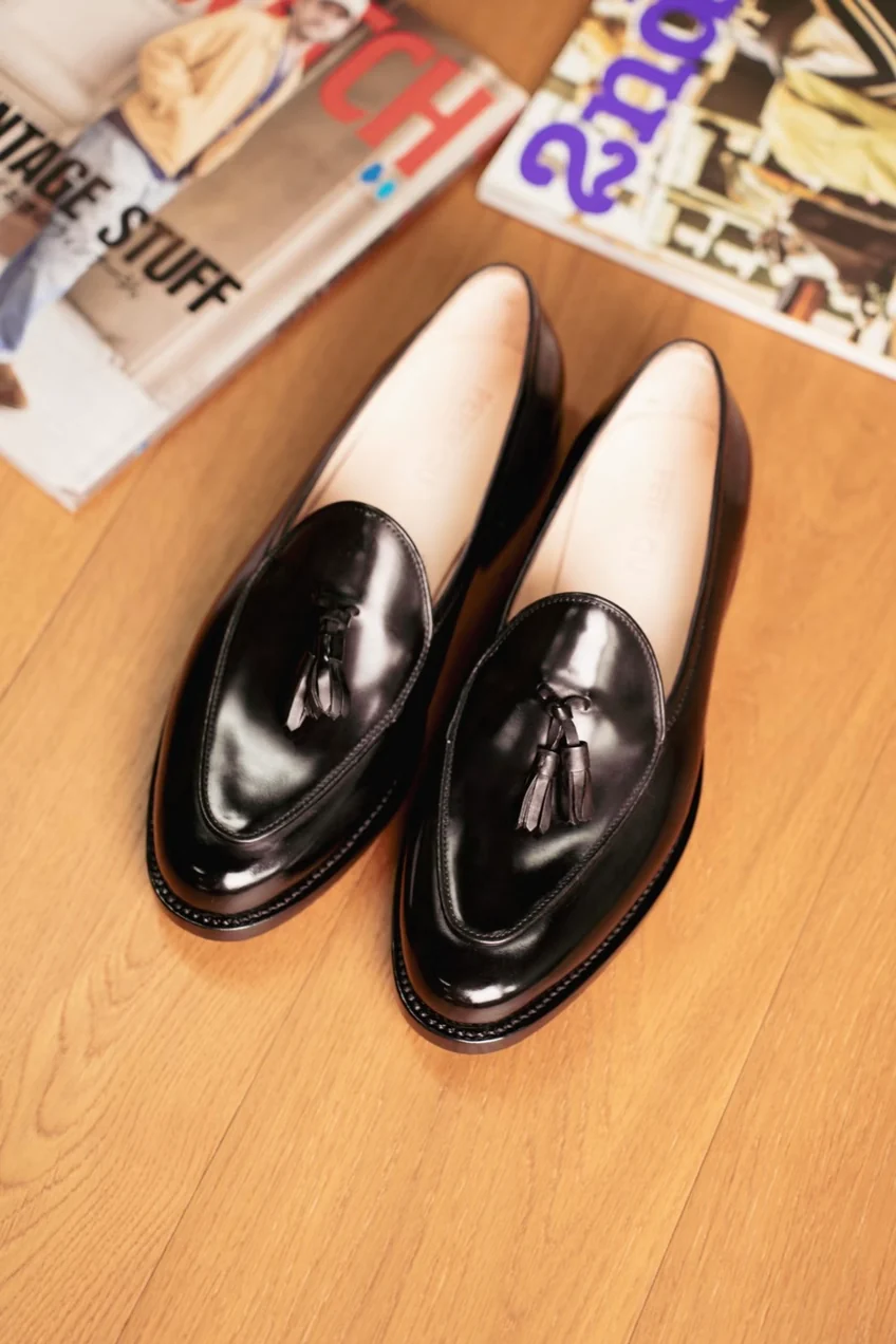 A pair of black cordovan loafers with tassels, displayed on a wooden surface.