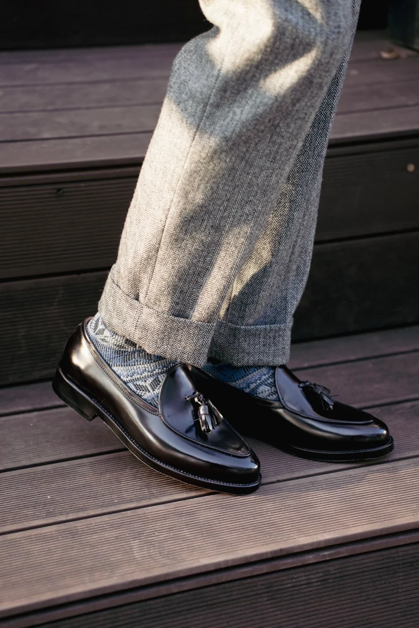 Black cordovan loafers with tassels paired with gray houndstooth pants and patterned socks.