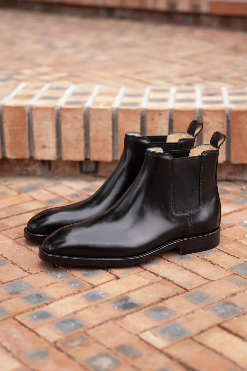 A pair of sleek black cordovan Chelsea boots with elastic side panels.