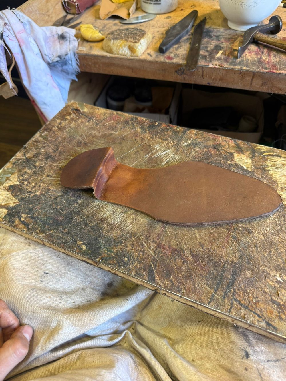 A brown leather shoe insole rests on a workbench covered with tools and materials.