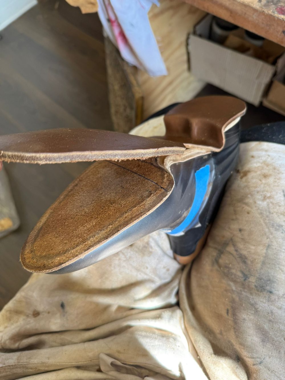A close-up of a partially constructed shoe with a brown leather upper and a black sole, resting on a fabric surface.