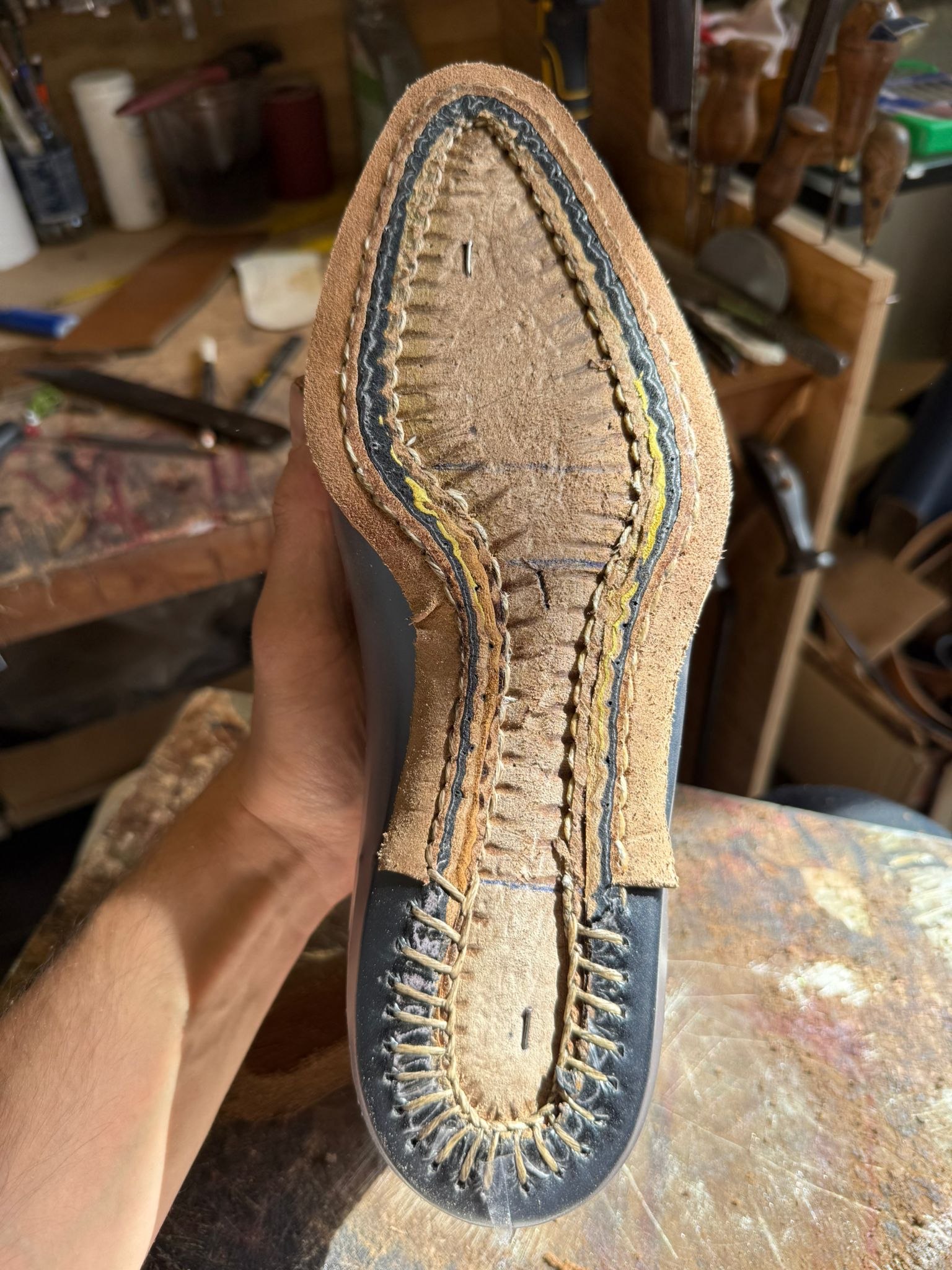 A close-up of a handcrafted shoe sole, featuring intricate stitching and a smooth black rubber edge.