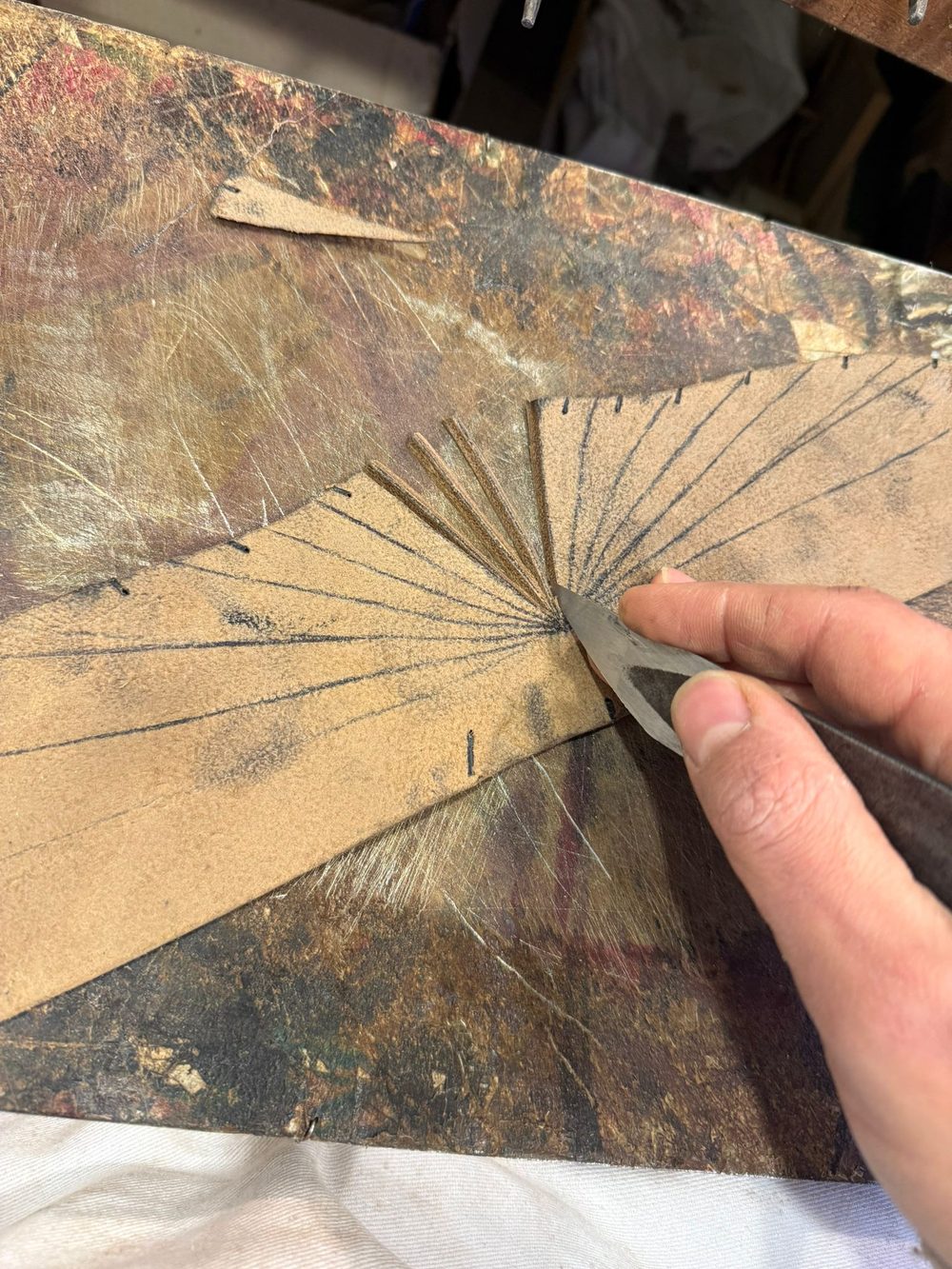 A hand holding a knife is cutting leather with marked lines for shoemaking.