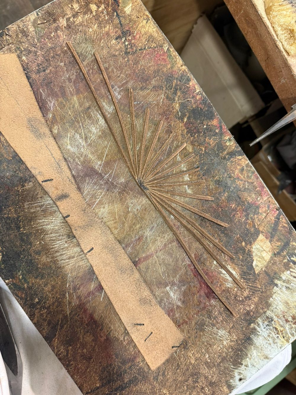 A piece of brown leather with thin strips arranged in a fan shape on a textured work surface.