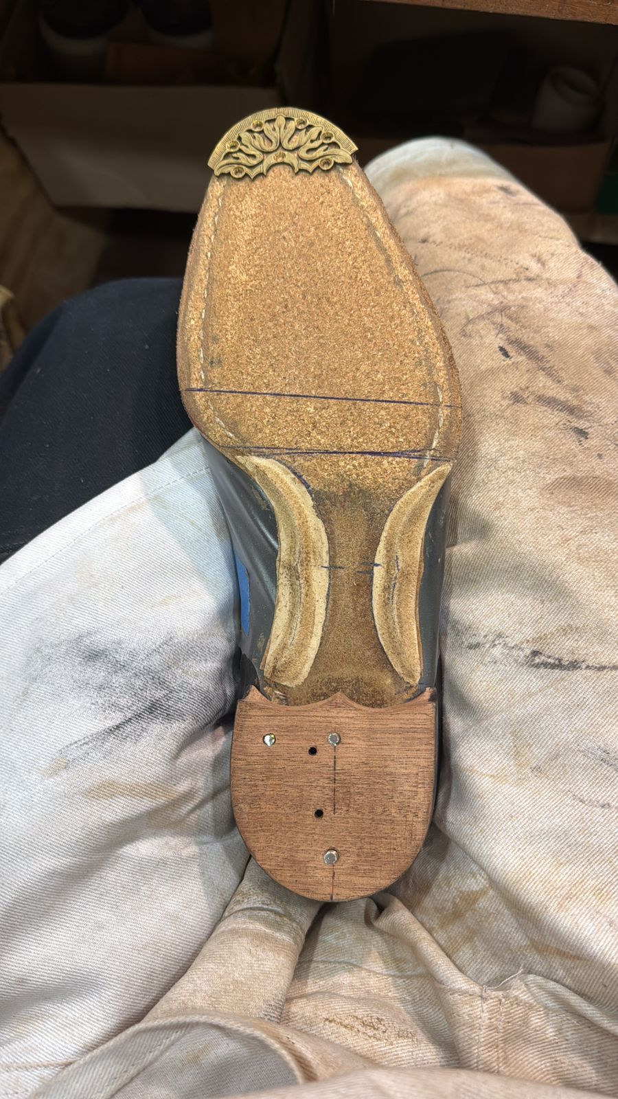 A close-up of the bottom of a shoe sole featuring a decorative brass piece and a wooden heel.