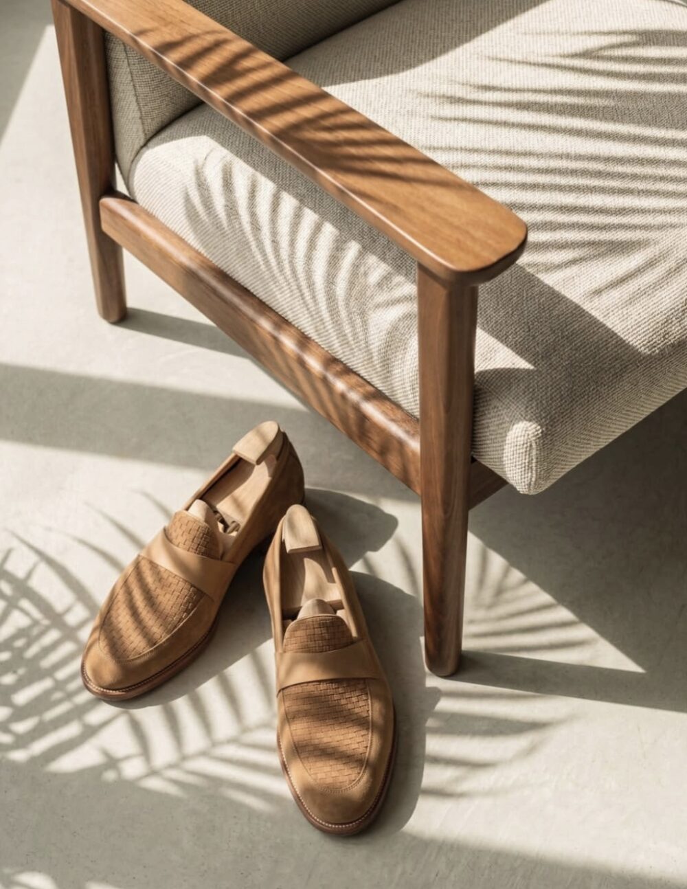 A pair of tan leather Amalfi loafers with woven details rests on a light surface beside a wooden chair.