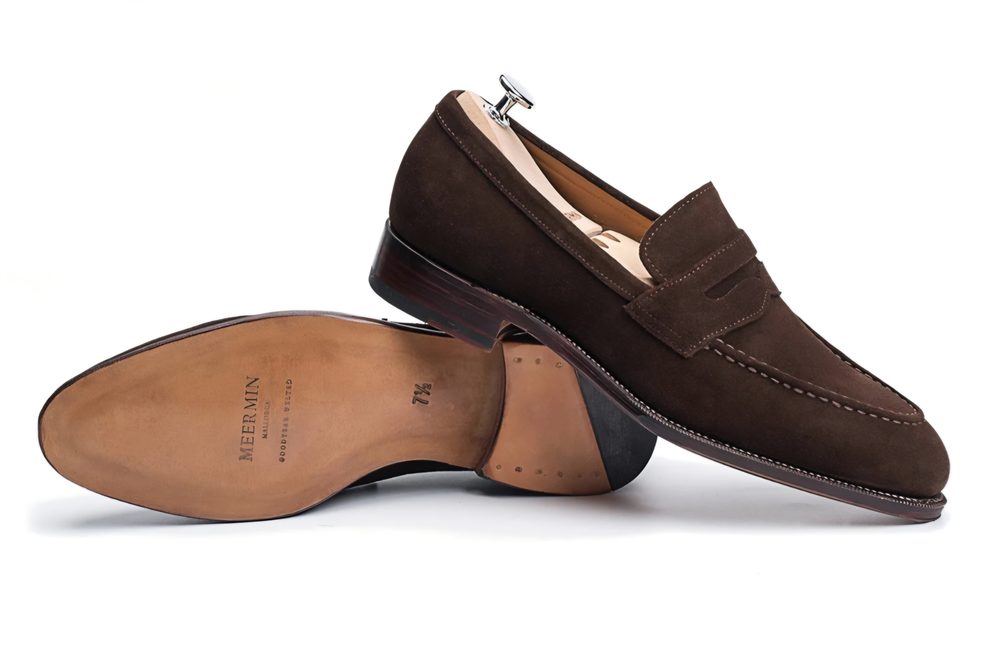 Brown suede loafers with a wooden heel and a decorative strap.