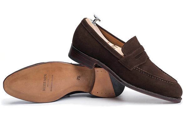 Brown suede loafers with a wooden heel and a decorative strap.