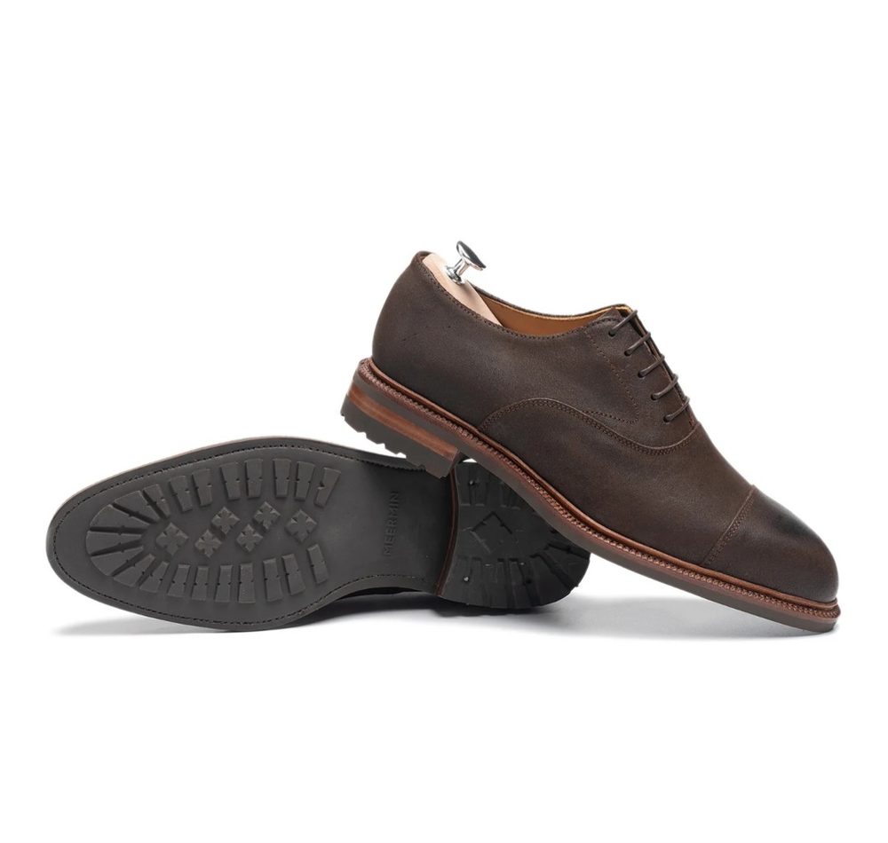A pair of brown leather dress shoes with a rubber sole and laces, displayed from the side and slightly angled.