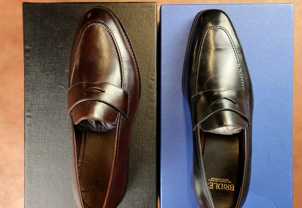 A brown leather loafer is on the left and a black leather loafer is on the right, each resting on their respective boxes.