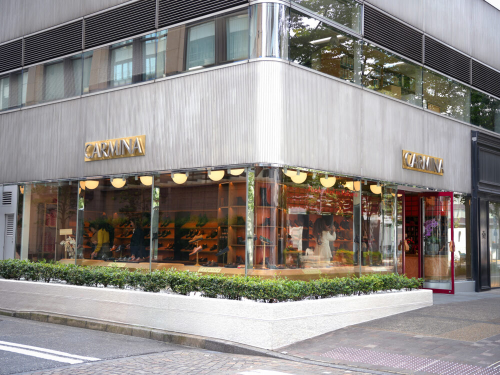 Storefront of Carmina Shoemaker featuring a glass façade, gold signage, and displayed shoes.