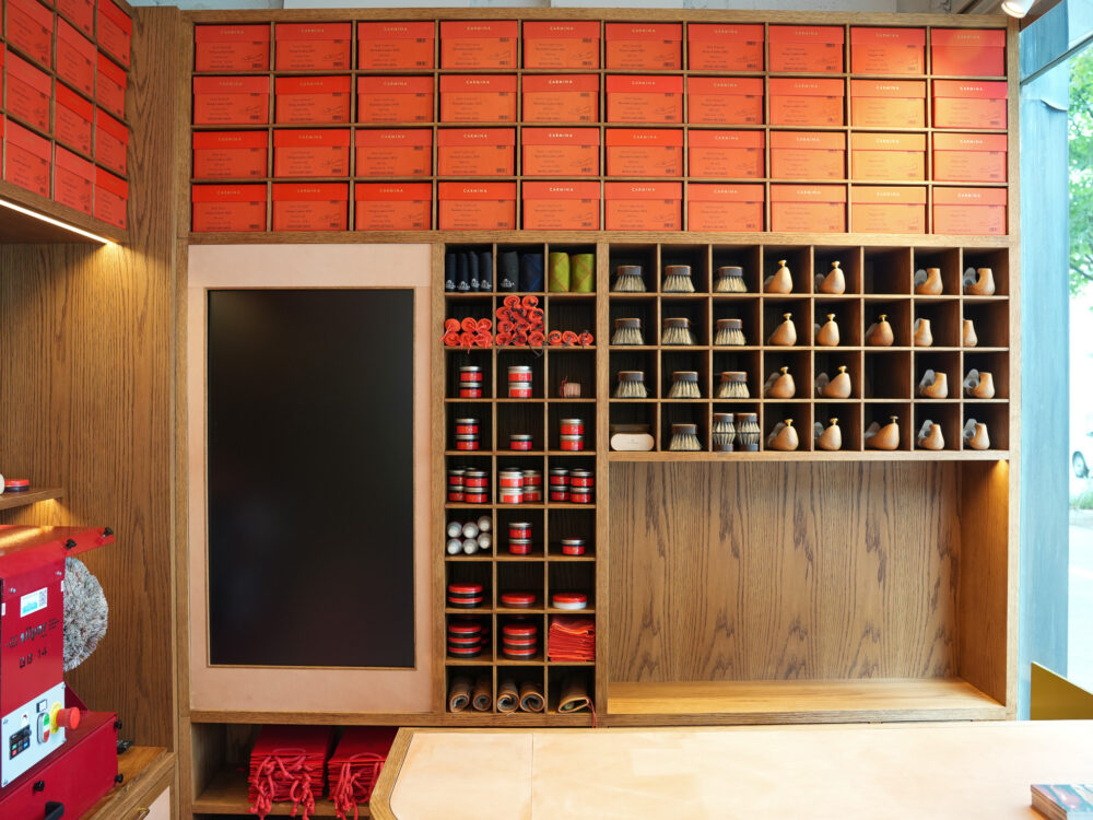 A wooden display wall filled with red shoeboxes and various shoe care items, including brushes and wooden birds.