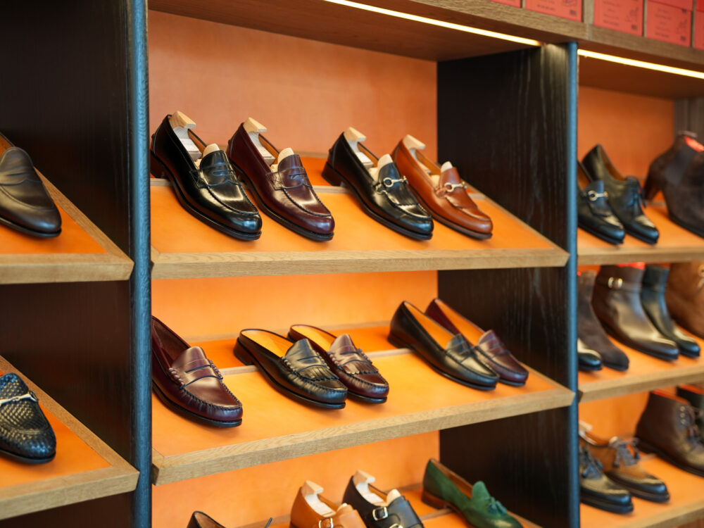 A display of men's leather shoes in various colors, including black, brown, and burgundy, arranged on wooden shelves.