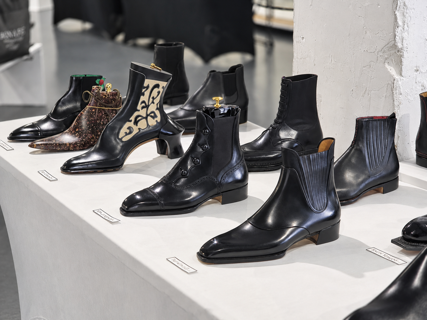 A collection of ten stylish black leather boots displayed on a table, showcasing various designs and decorative elements.
