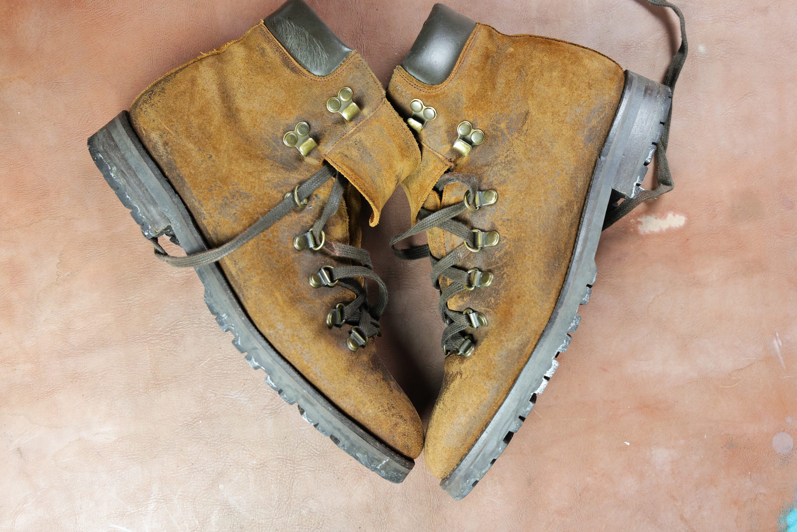 A pair of worn brown leather boots with metal eyelets and laces, suitable for restoration with Saphir Oiled Leather Cream.