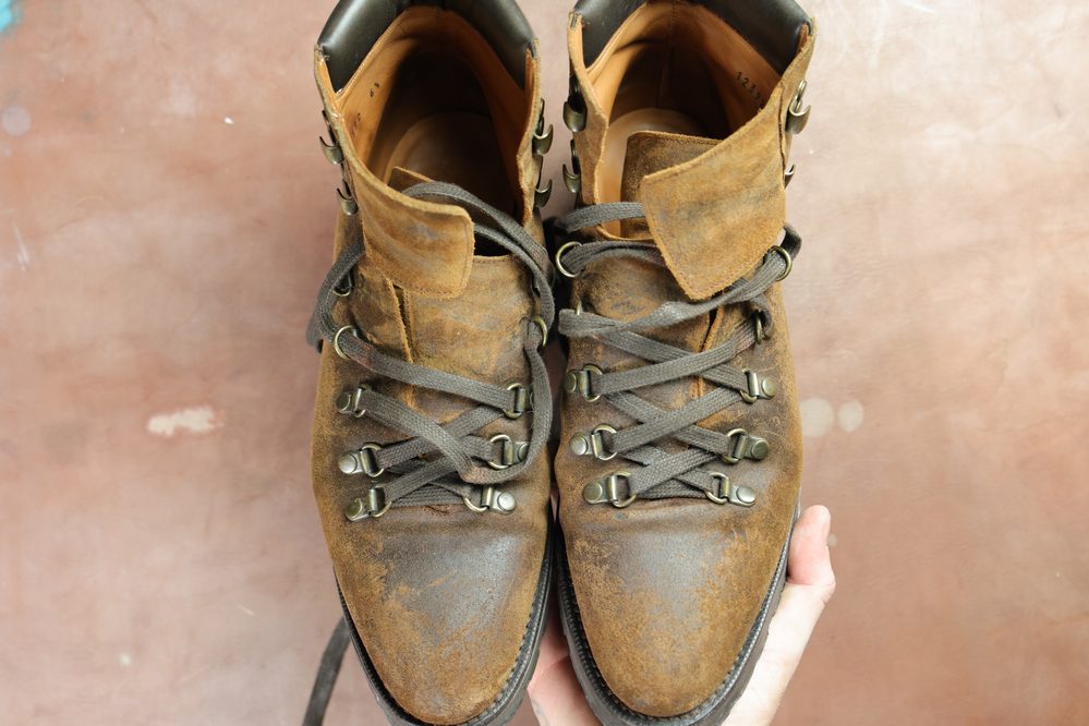 A pair of worn brown leather boots with gray laces, ready for restoration using Saphir Oiled Leather Cream.