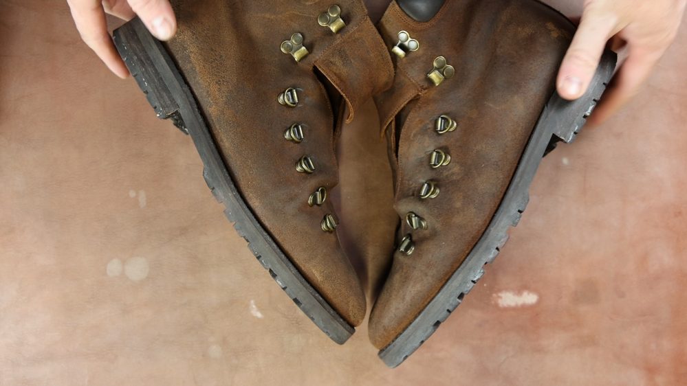 A pair of worn brown leather boots with brass eyelets and a black rubber sole, ready to be treated with Saphir Oiled Leather Cream.