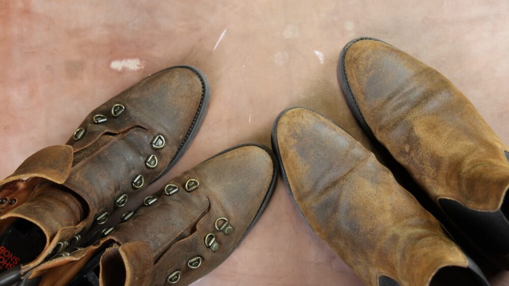 Two pairs of worn brown leather boots, one with decorative metal eyelets, ready for restoration with Saphir Oiled Leather Cream.