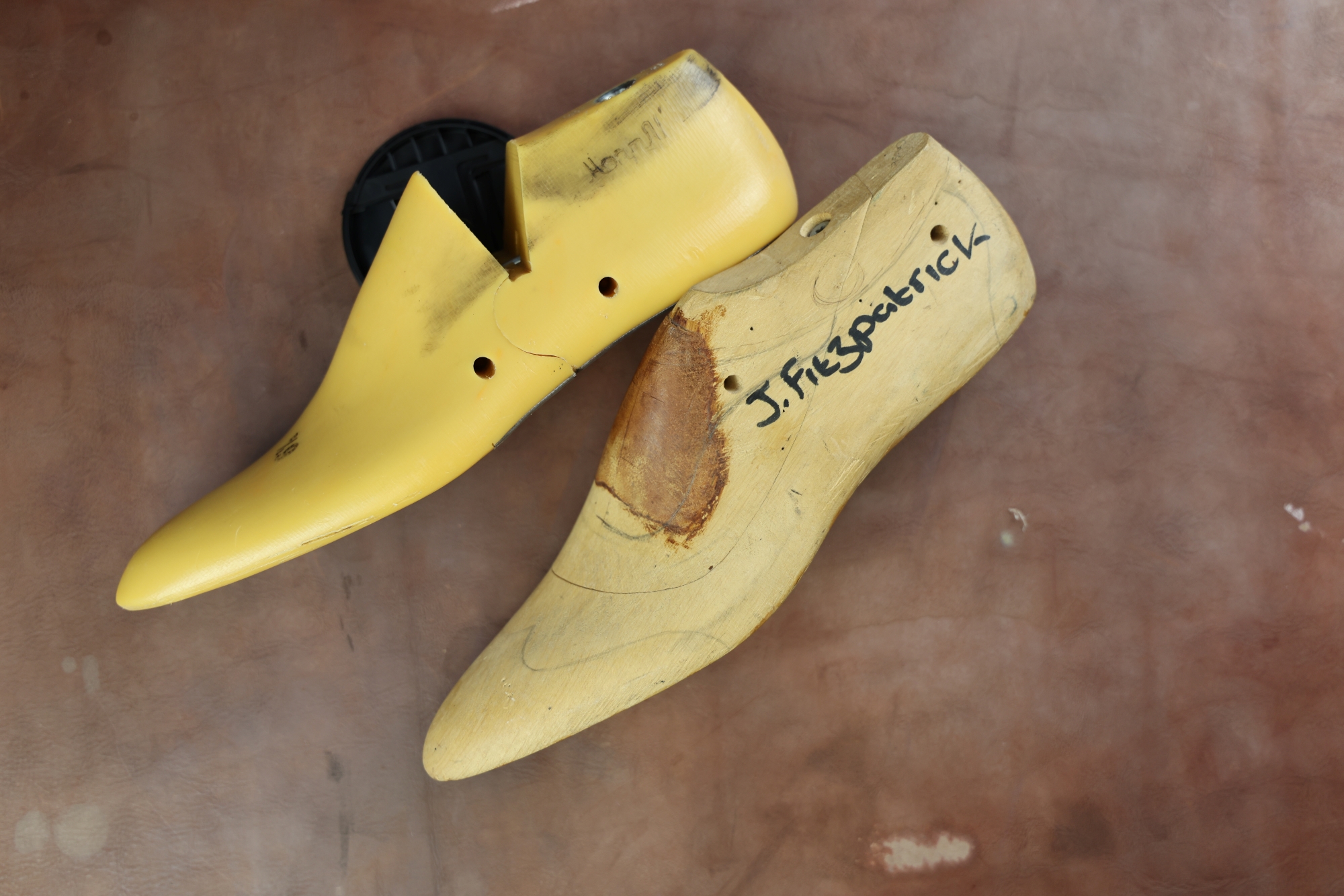 A yellow shoe last and a wooden shoe last with handwritten names and markings.