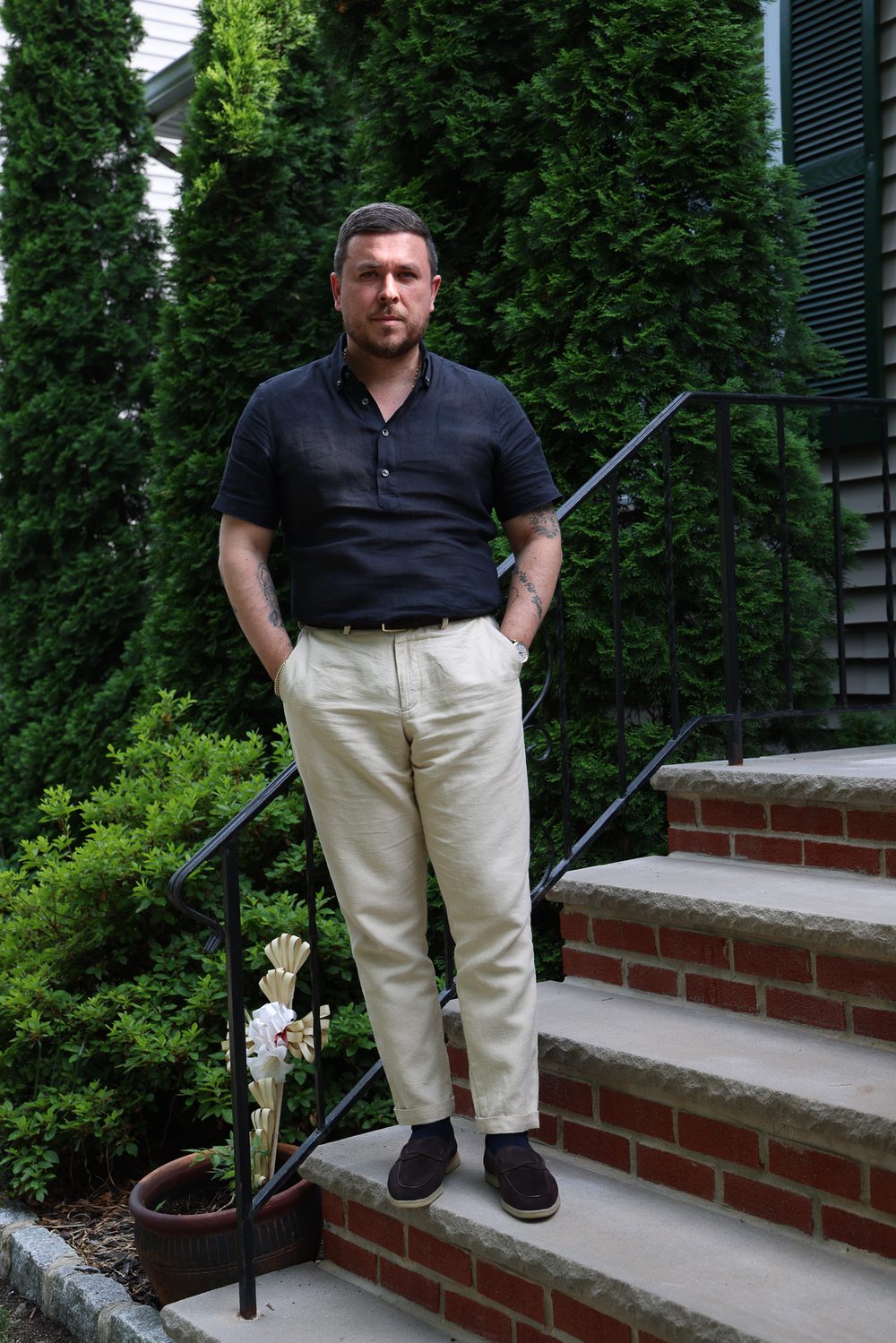 A man in a dark short-sleeve shirt and light-colored pants stands on stone steps next to green shrubs, reflecting the theme of "My New Chapter."