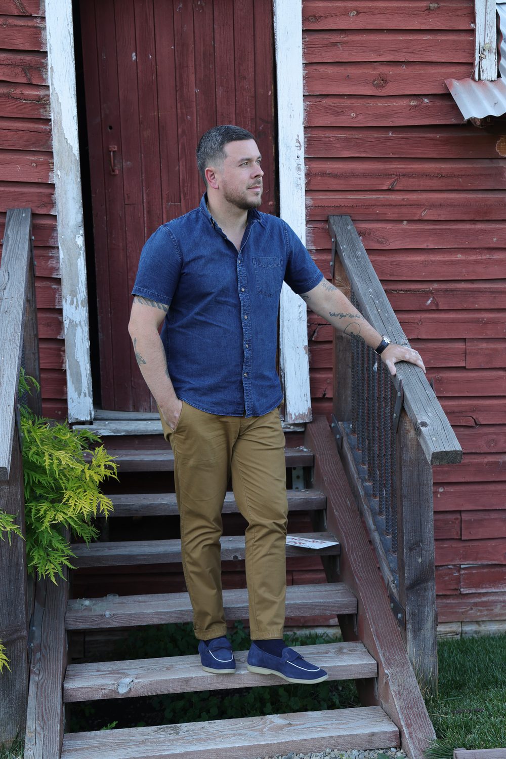 A man in a blue button-up shirt and khaki pants stands on wooden steps, embodying the theme of "My New Chapter."