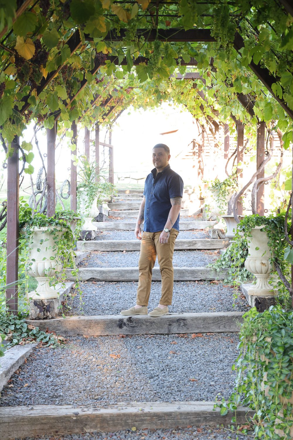 A man stands on stone steps surrounded by lush green vines and planters, embodying the theme of "My New Chapter."