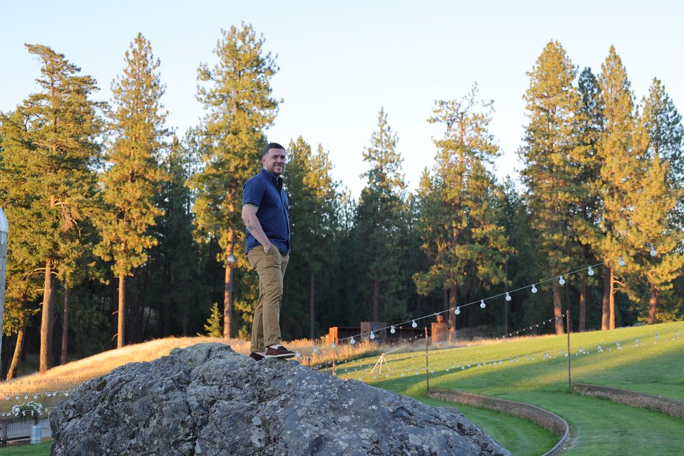 A man stands confidently on a large rock, wearing a navy shirt and tan pants, as part of "My New Chapter."