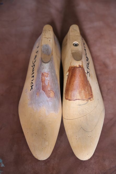 Two wooden shoe lasts, one with a worn, light-colored finish and the other featuring a darker, polished area, illustrating what is a shoe last.