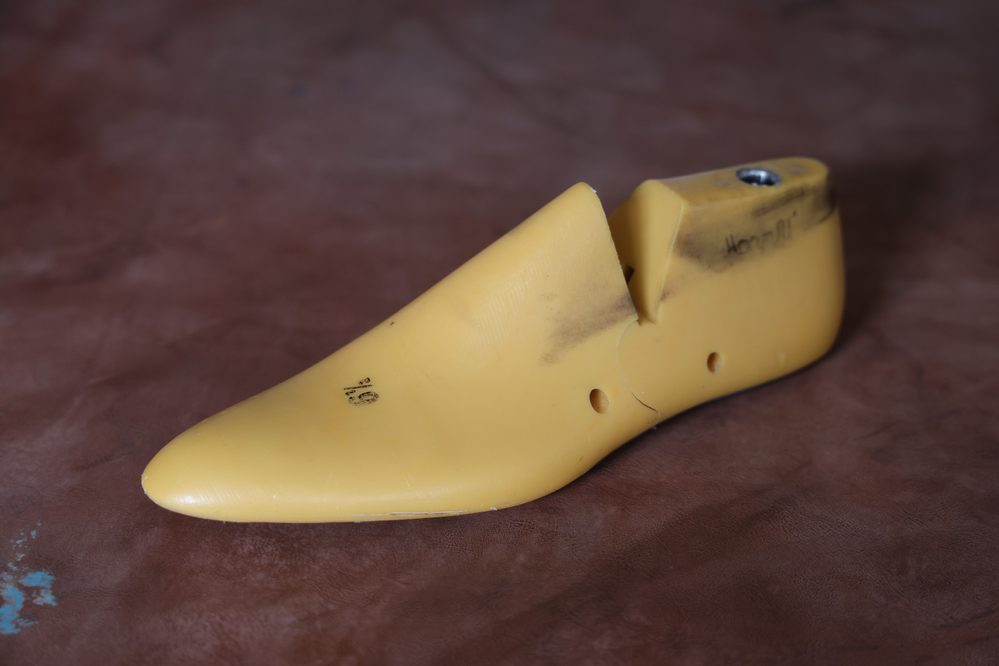 A yellow shoe last, used in footwear design, is shown at an angle with visible markings and cutouts.
