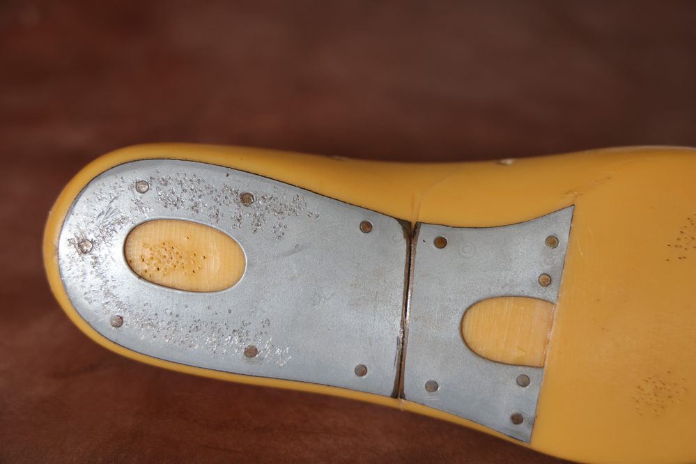 A close-up of a yellow shoe last featuring a silver metal plate with holes, illustrating what is a shoe last.