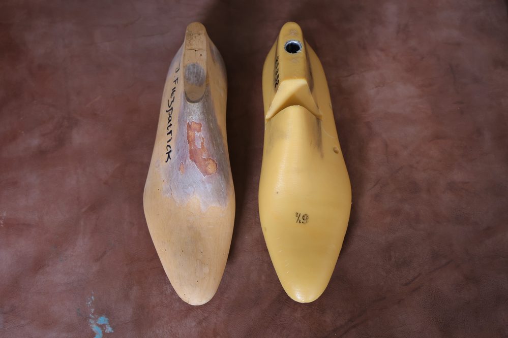 Two shoe lasts are shown: one is a worn wooden last with markings, and the other is a smooth yellow plastic last, illustrating what is a shoe last.