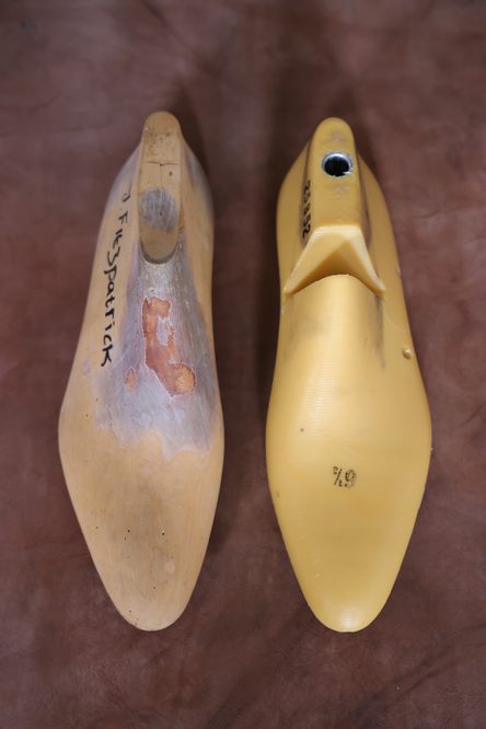 Two shoe lasts, one wooden and worn with a rough surface and the other smooth and yellow plastic, illustrate what is a shoe last.