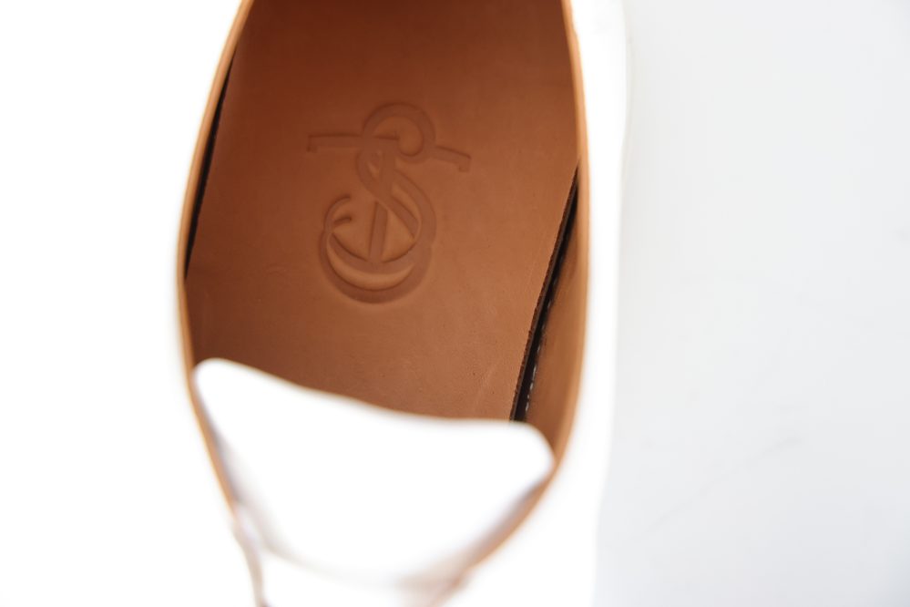 Close-up of the interior of the Olympia White Calf Sneaker, featuring a tan insole embossed with a logo.