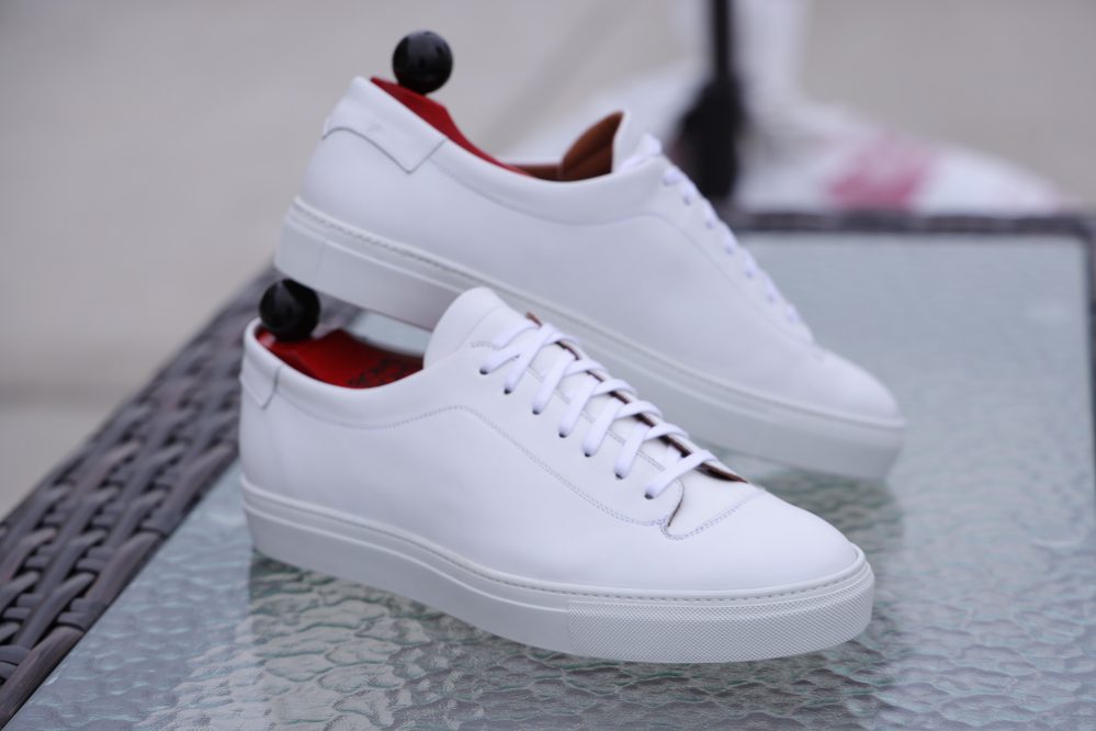 A pair of white leather Olympia White Calf Sneakers with red insoles and white laces.