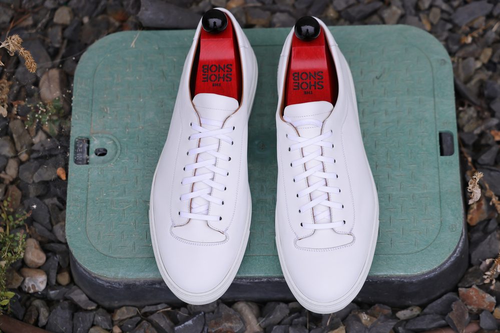 A pair of white leather Olympia White Calf Sneakers with black eyelets and red insoles, viewed from above.
