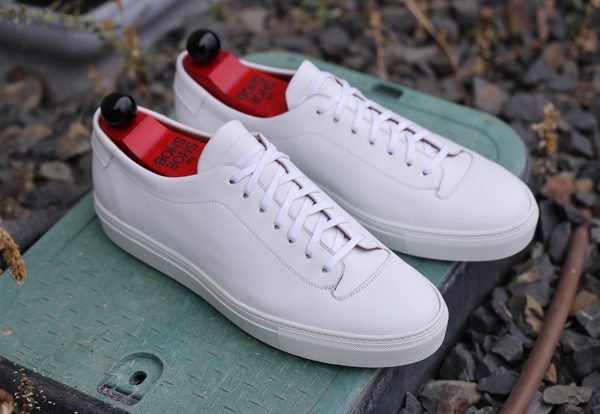A pair of white leather Olympia White Calf Sneakers with red insoles and white laces.
