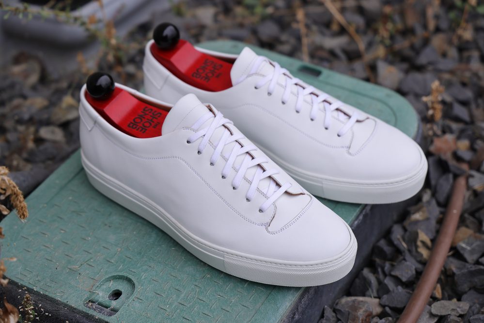 A pair of white leather Olympia White Calf Sneakers with red insoles and white laces.