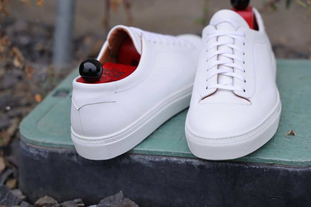 Close-up of the Olympia White Calf Sneaker featuring a smooth white leather exterior and a red interior lining.